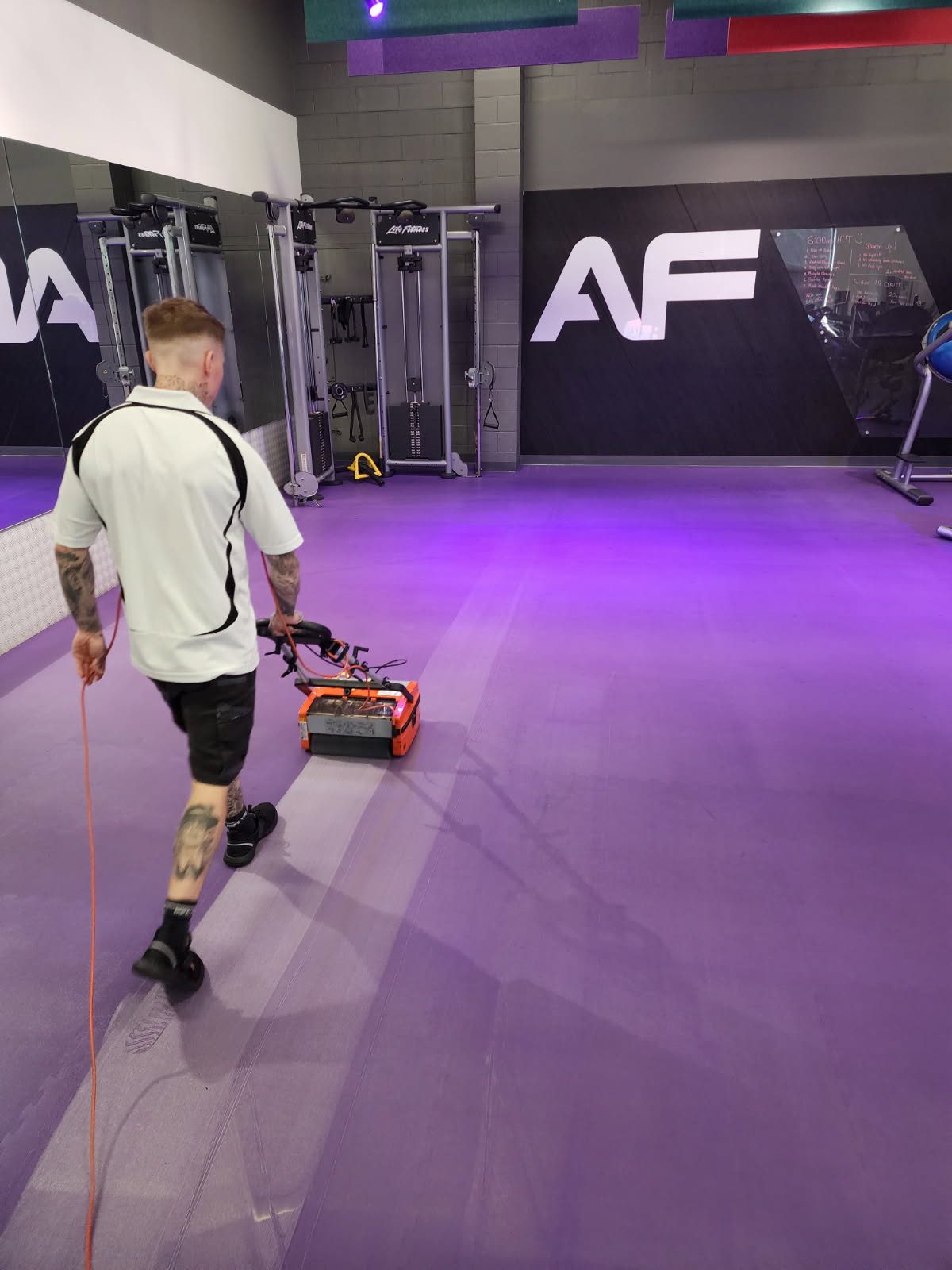 Cleaner using professional floor-cleaning equipment in a commercial gym